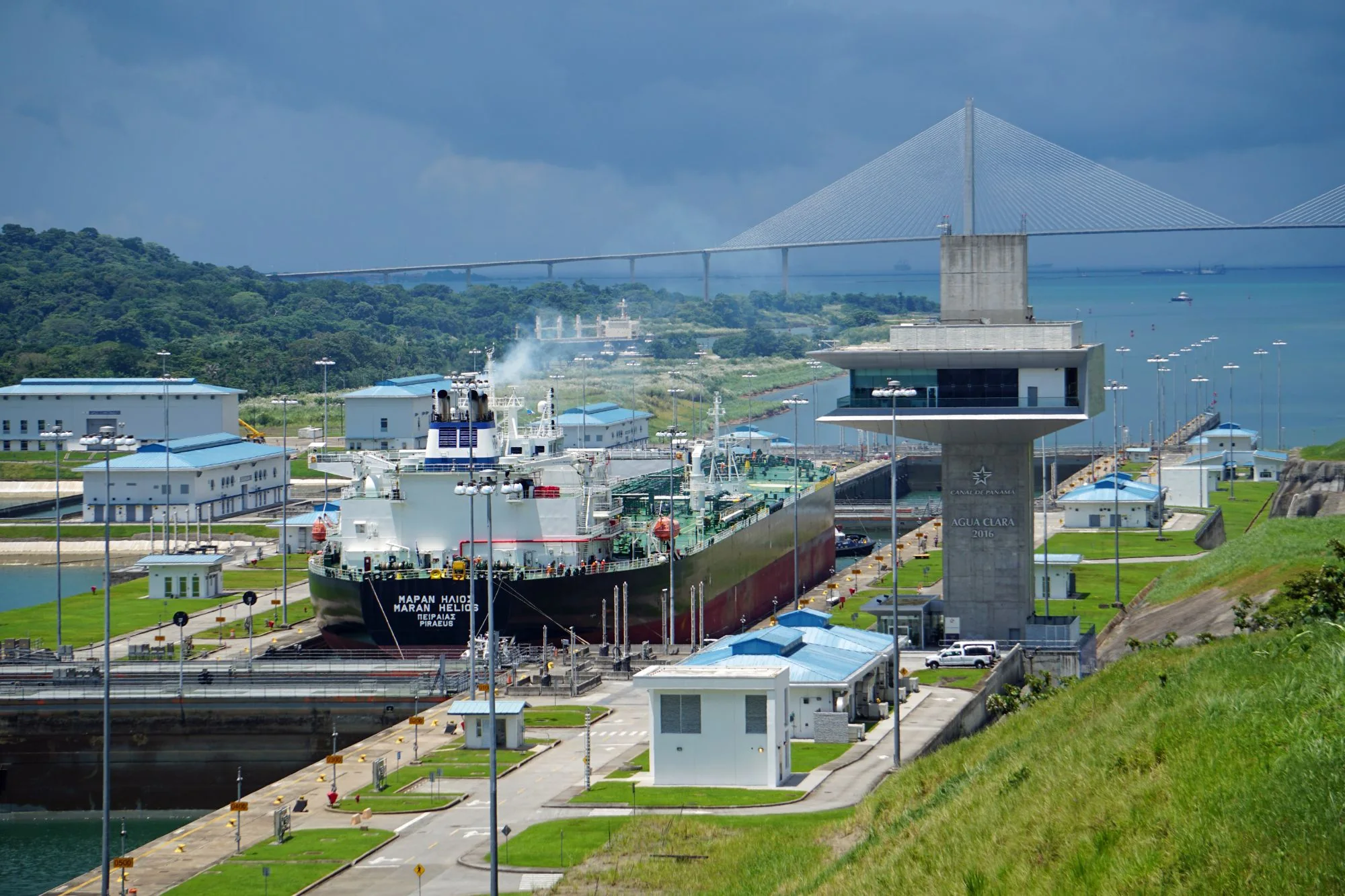 Buque cruzando las esclusas de Agua Clara del Canal de Panamá, con selva, mar y un puente atirantado al fondo